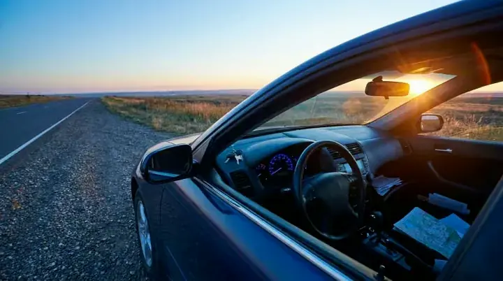 A parked car on an empty road shoulder at dusk with keys on the dashboard