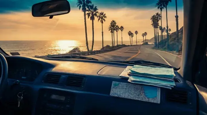 A coastal highway with palm trees seen through a windshield
